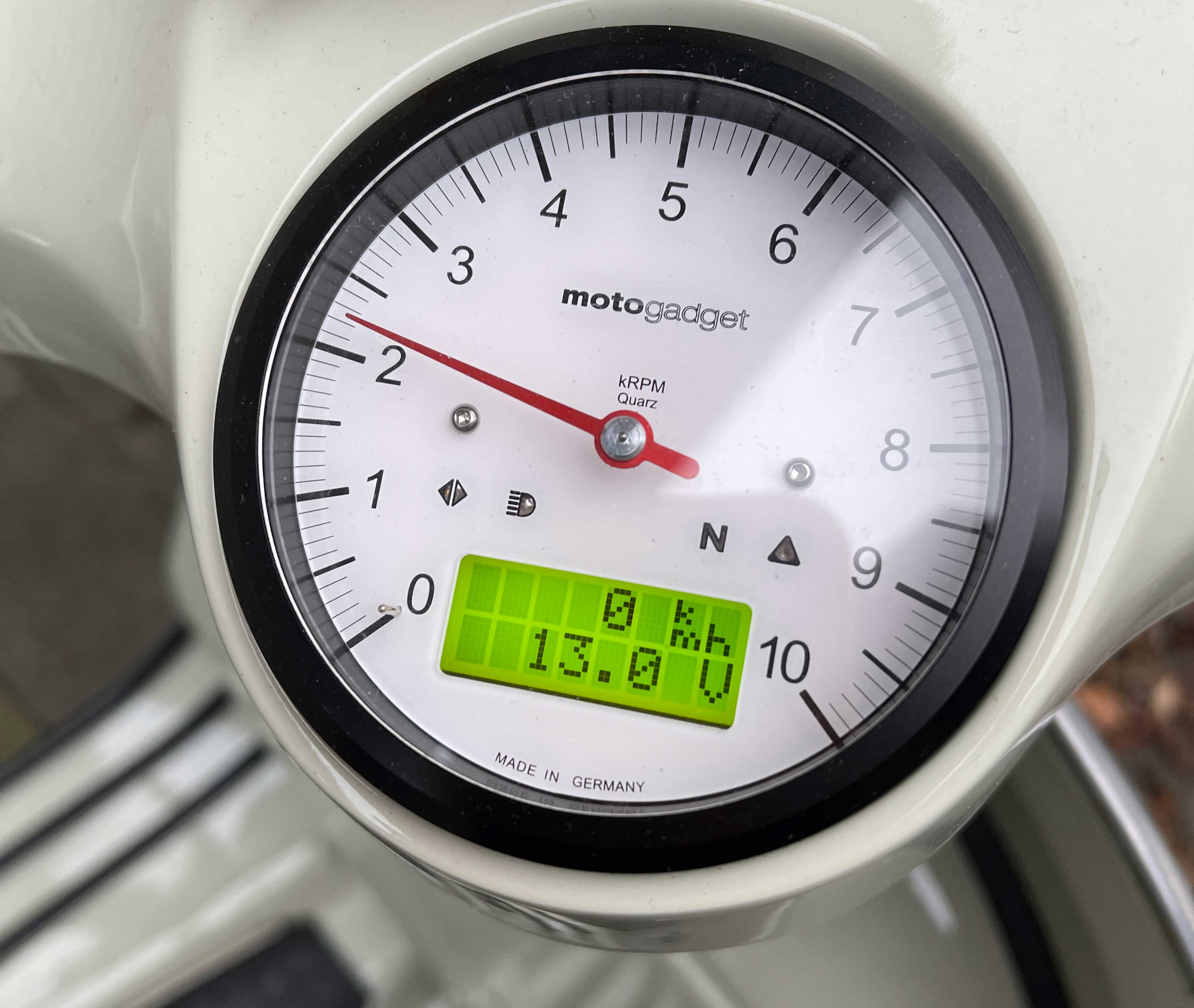 Motogadget Tachoanzeige mit rotem Zeiger bei 2 und digitaler Anzeige mit 0 km/h und 13,0 V.